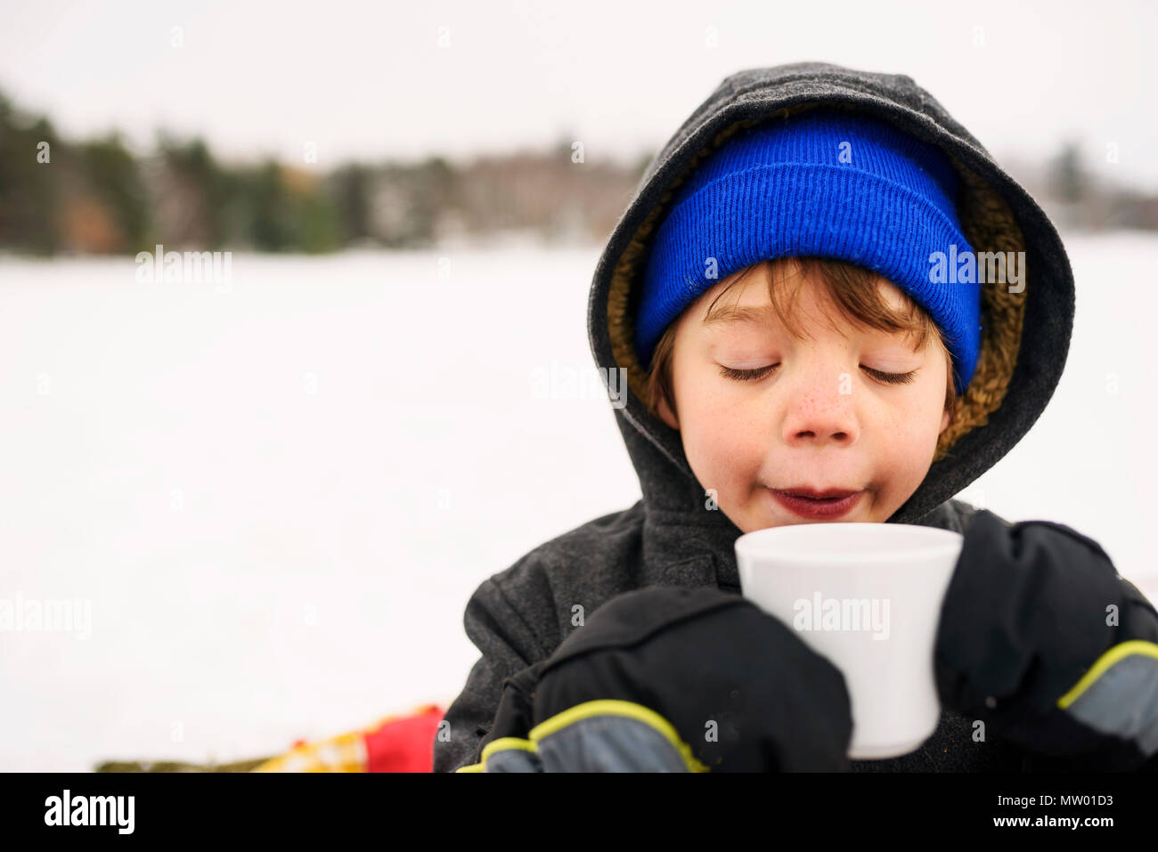 Boy standing in the snow drinking hot chocolate Stock Photo