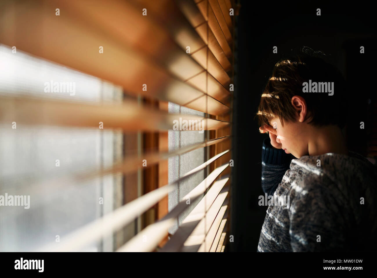 Tired Boy standing by a window rubbing his eyes Stock Photo