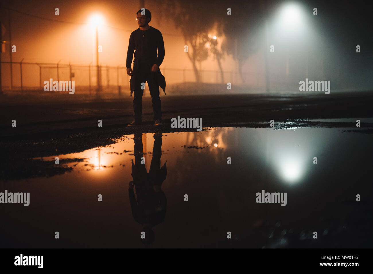 Man standing in the road by a puddle of water at night, California, United States Stock Photo