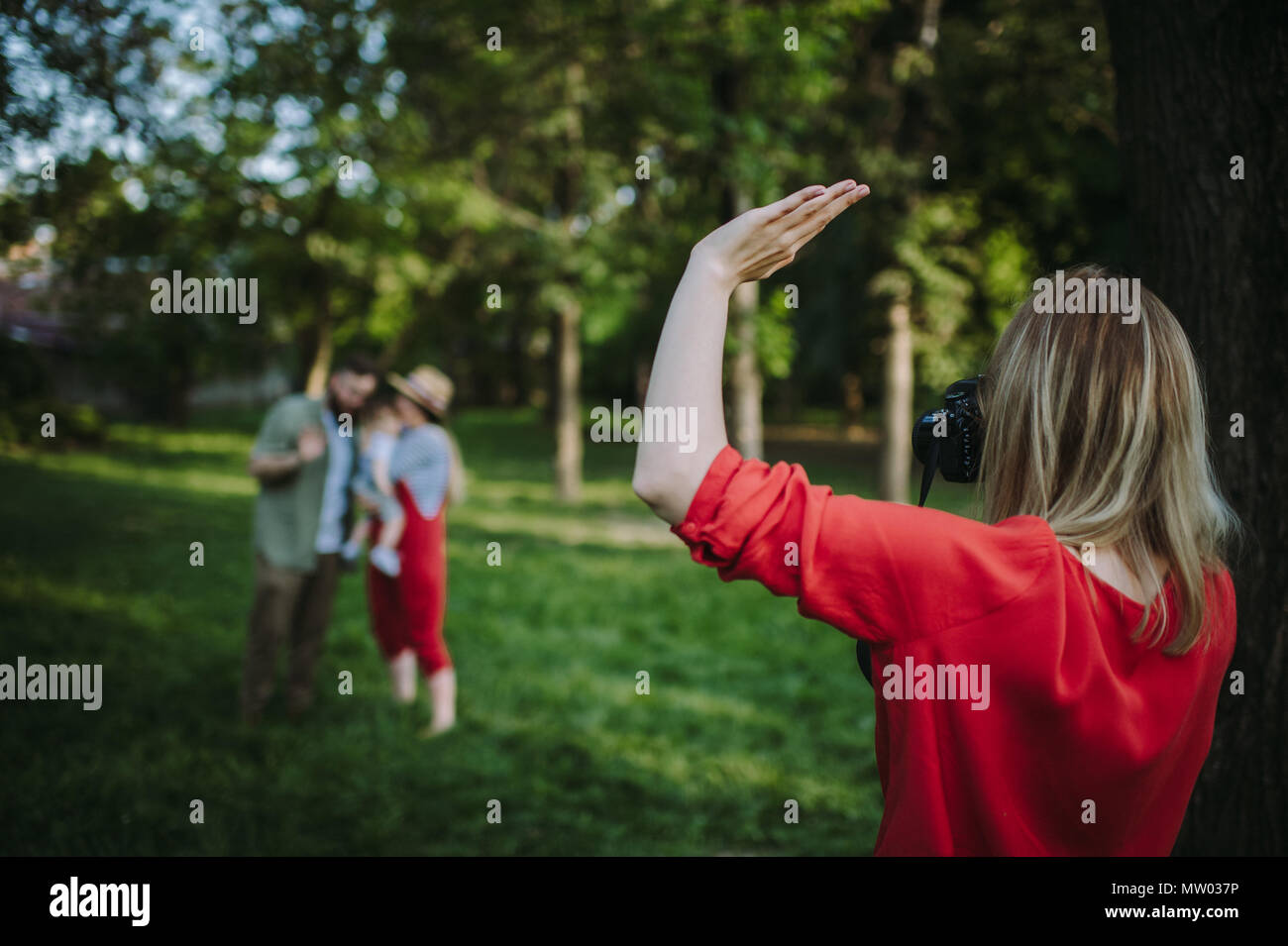 Woman standing in park waving at a mother and father with their son Stock Photo