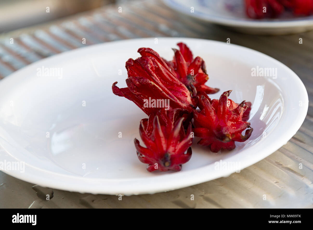 Roselle (Hibiscus sabdariffa) magenta color fresh calyces (sepals) on white plate, washstand outdoors Stock Photo