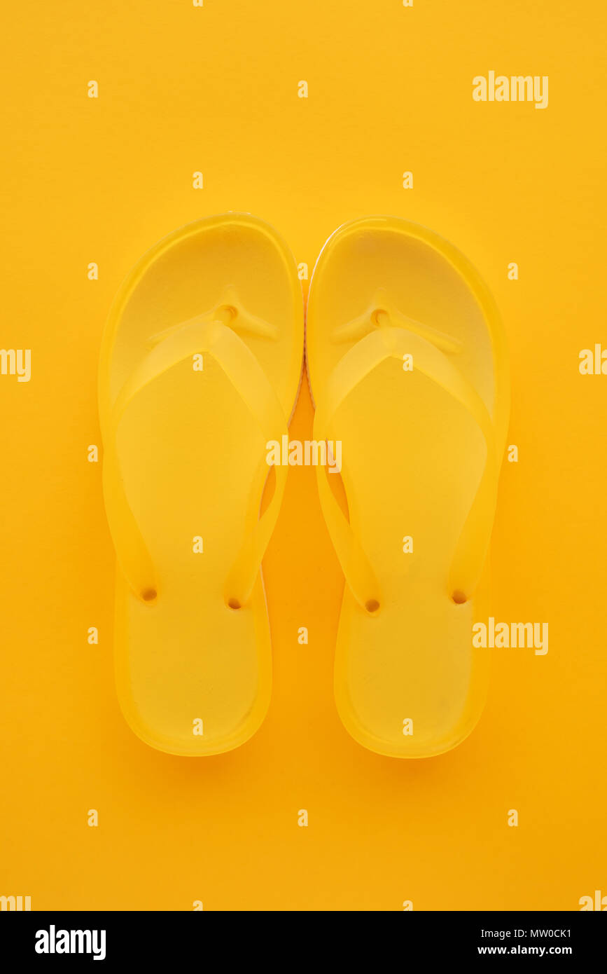 Top view of yellow flip flops pair on same color background with copy space. Beach sandals or slippers in minimalistic warm summer toned composition. Stock Photo