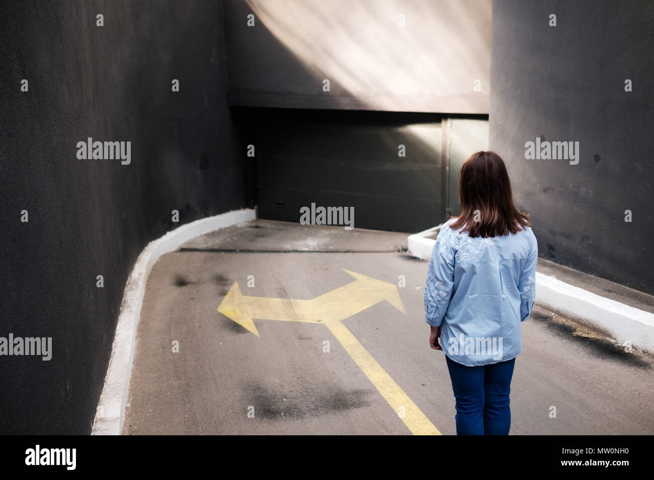Firl standing near two arrows printed on grunge road, making decision Stock Photo