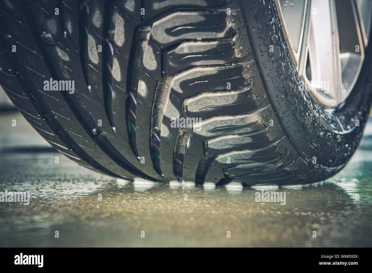 Brand New Vehicle Tire Tread Closeup Photo. Car Wheel on the Wet Pavement. Stock Photo