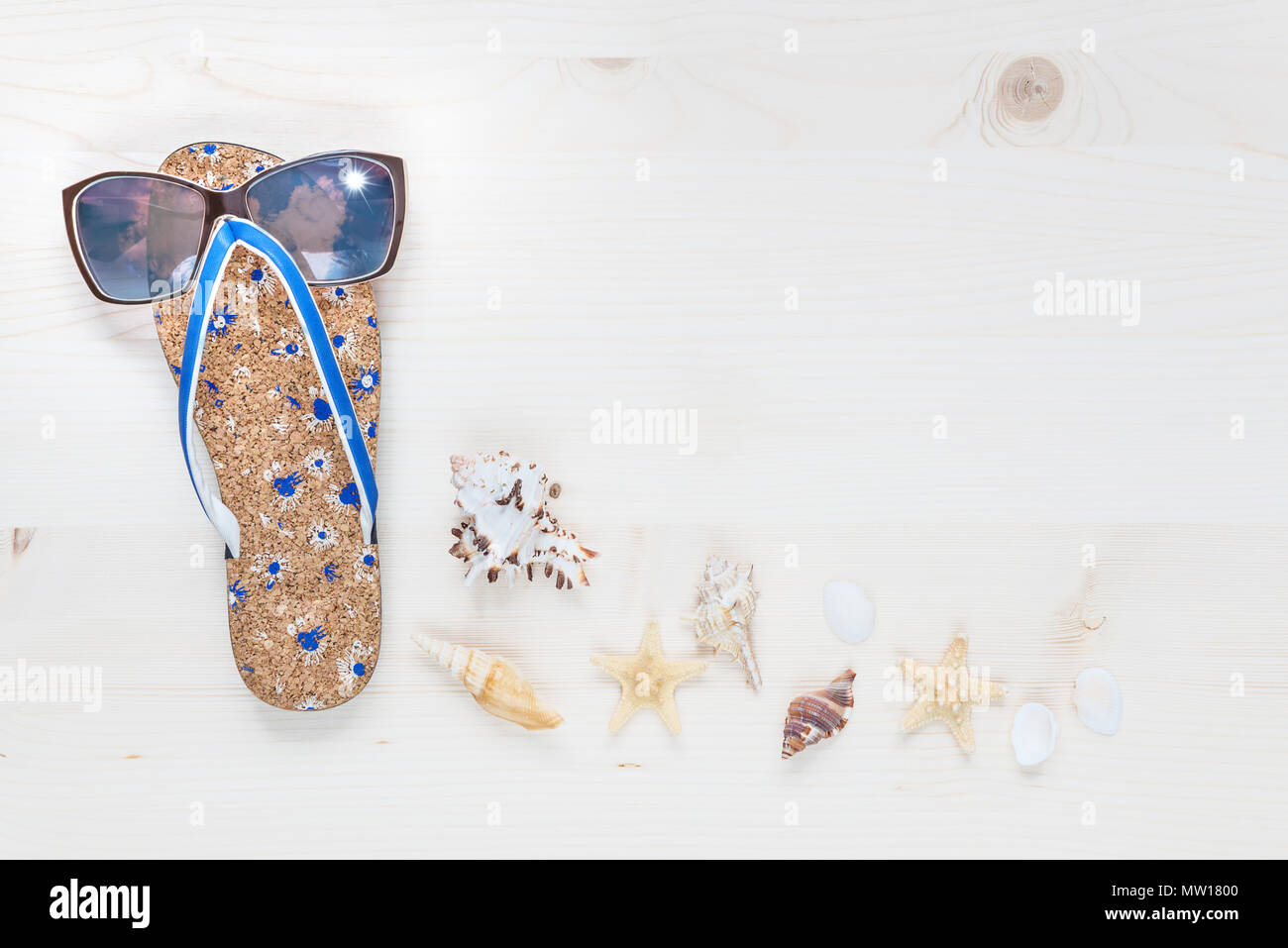 Concept of a beach holiday: slippers, sunglasses and seashells are on a light wooden surface. Top view, flat lay Stock Photo
