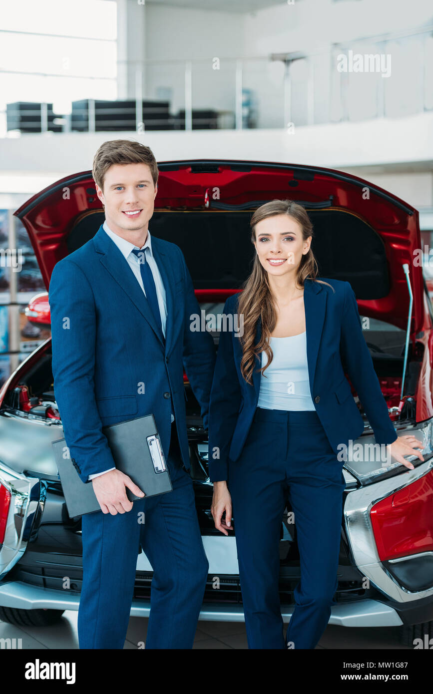 Sales managers posing in a car showroom near car with open hood Stock