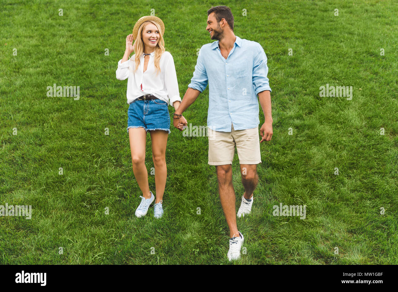 happy couple in love holding hands while walking on green lawn together ...