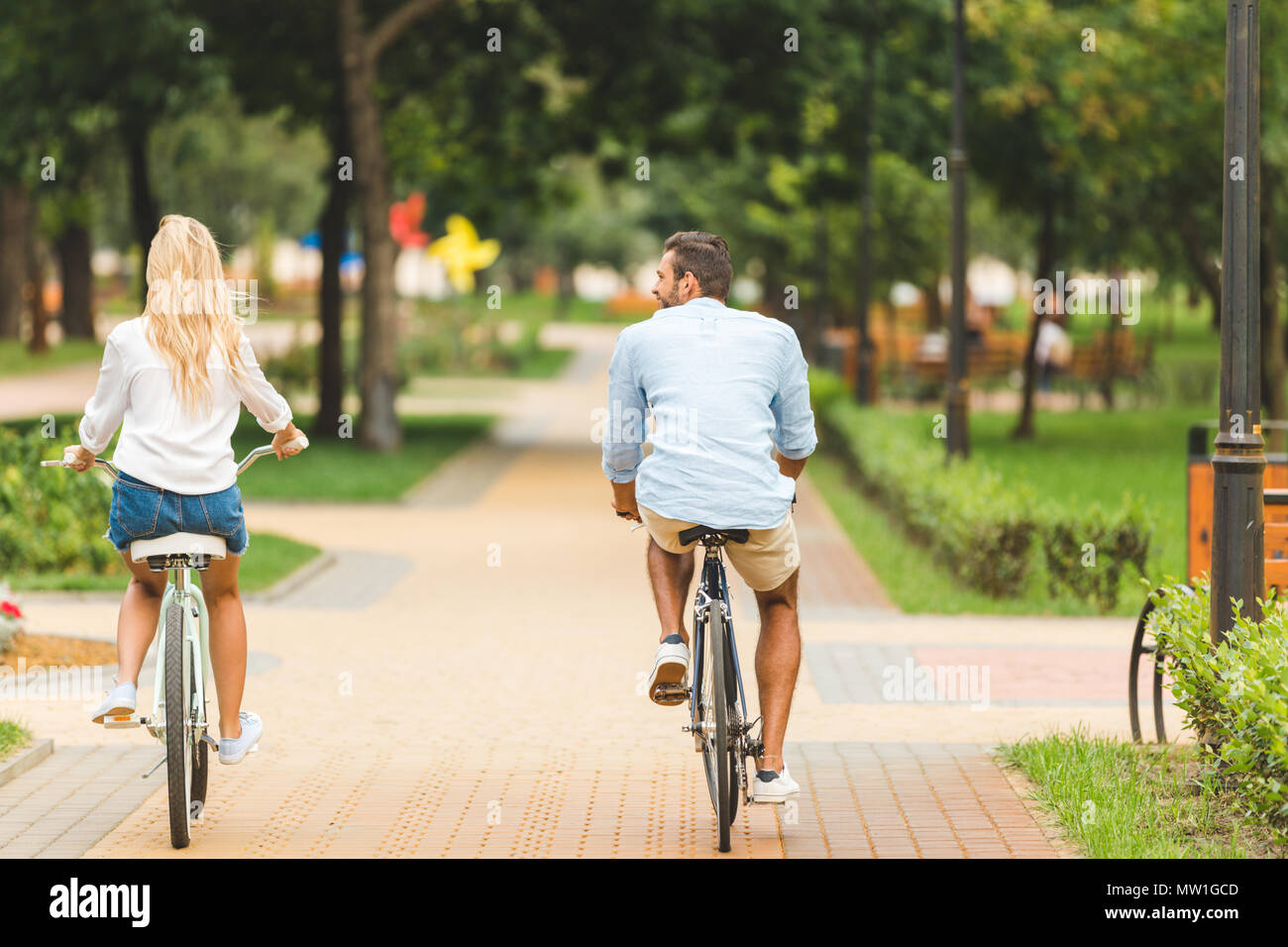 back view of stylish man and woman riding bicycles in park Stock Photo ...