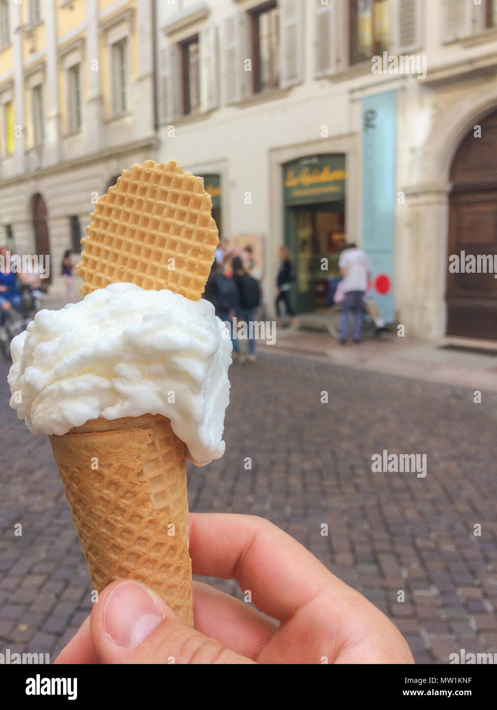 A male hand is holding a scoop of icecream in a cone topped with a ...