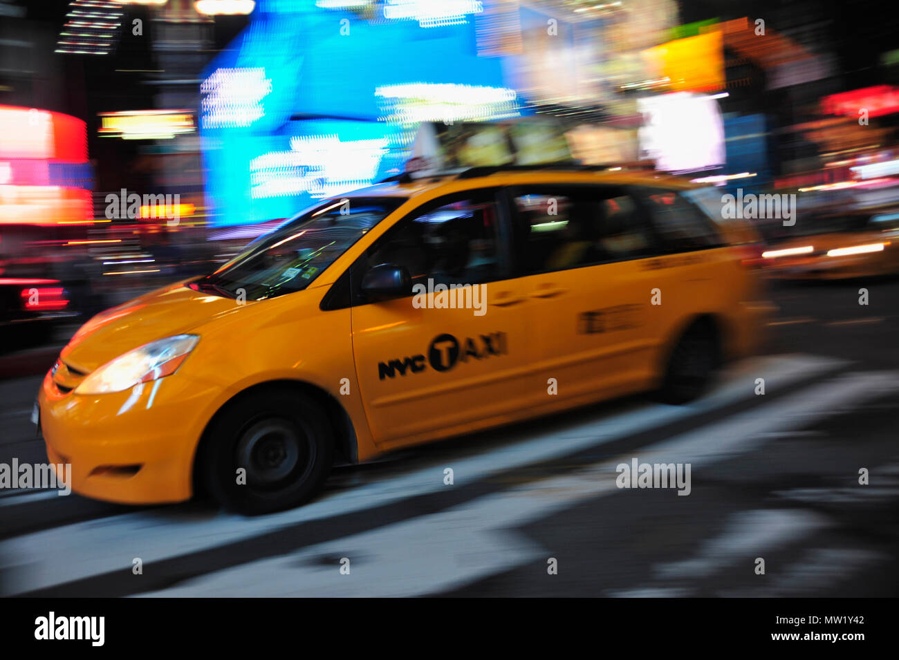 New York taxi van moving through Times Square with blur of lights beyond, New York, NY, USA Stock Photo