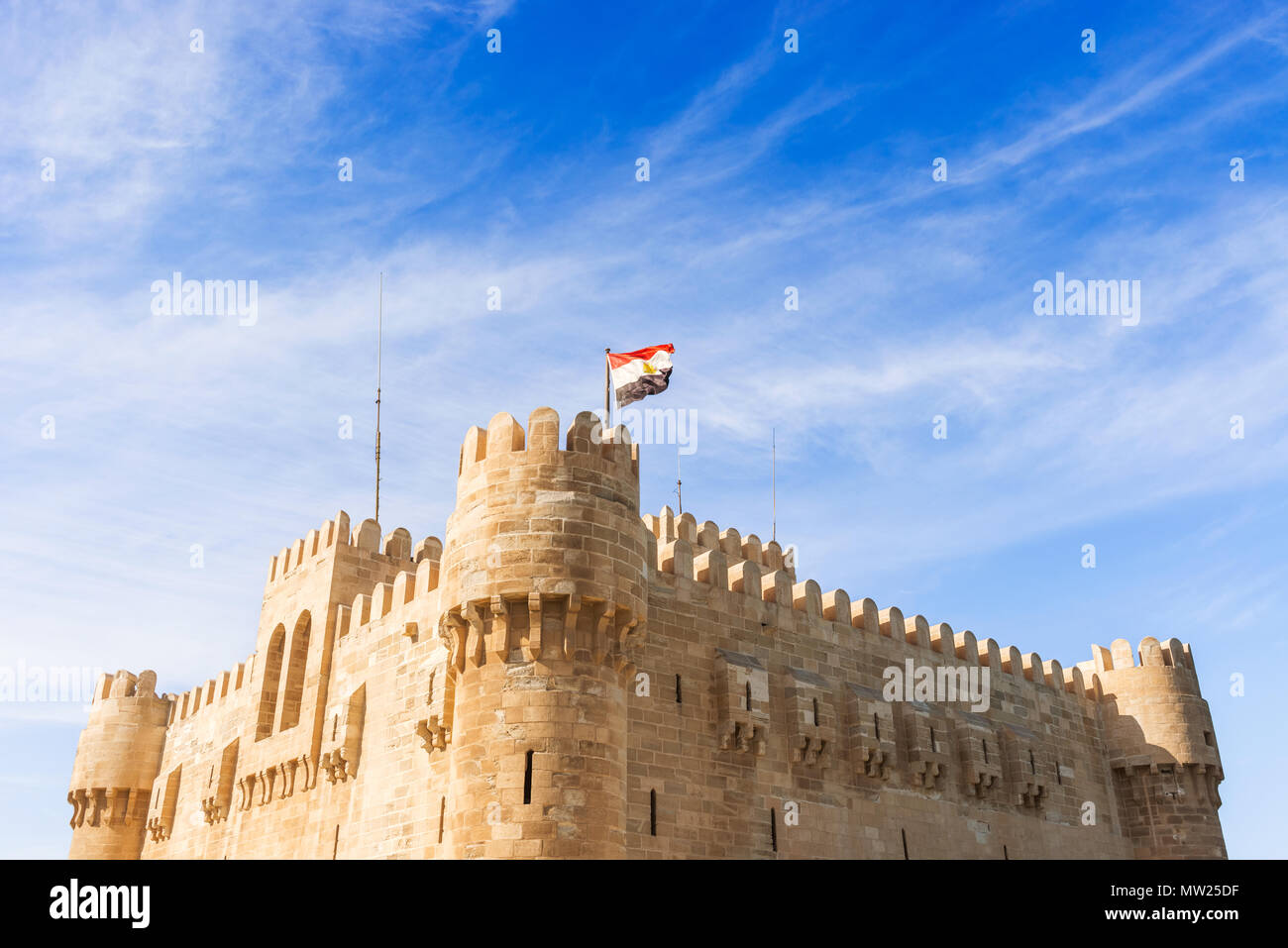 Photo of Qaitbay Castle or Citadel with Egyptian flag in Alexandria, Egypt. The Citadel of Qaitbay is a 15th-century defensive fortress on the Mediter Stock Photo