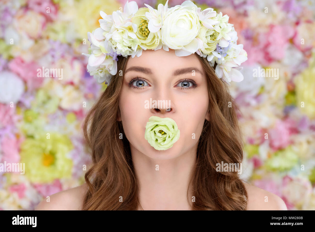 young woman in floral wreath with blossoming rose bud in mouth Stock