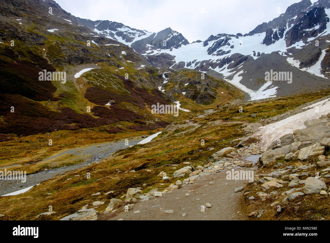 The hiking path towards the Martial Glacier near Ushuaia, Argentina, leads through patches of snow and next to a small stream towards a snowy glacier. Stock Photo