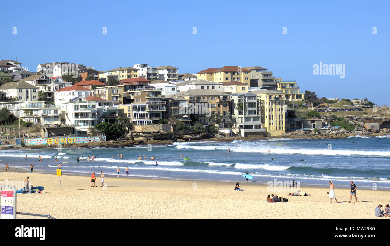 People enjoying sunny day at north side of Bondi beach in Sydney Australia. In view is Sydney cityscape of waterfront buildings or real estate. Stock Photo