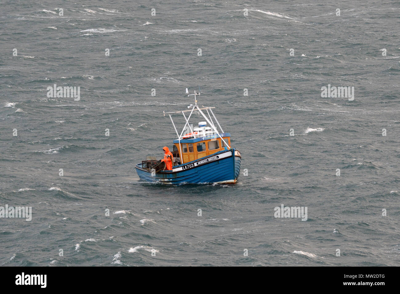 Small fishing boat at sea with 2 crew aboard picking up lobster baskets creel pot Stock Photo