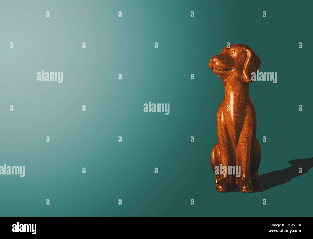 Wooden, gold doggy figurine. The wooden dog looks up with a satisfied face. A view of a dog who sits on a dark pastel background. Animal concept. Stock Photo