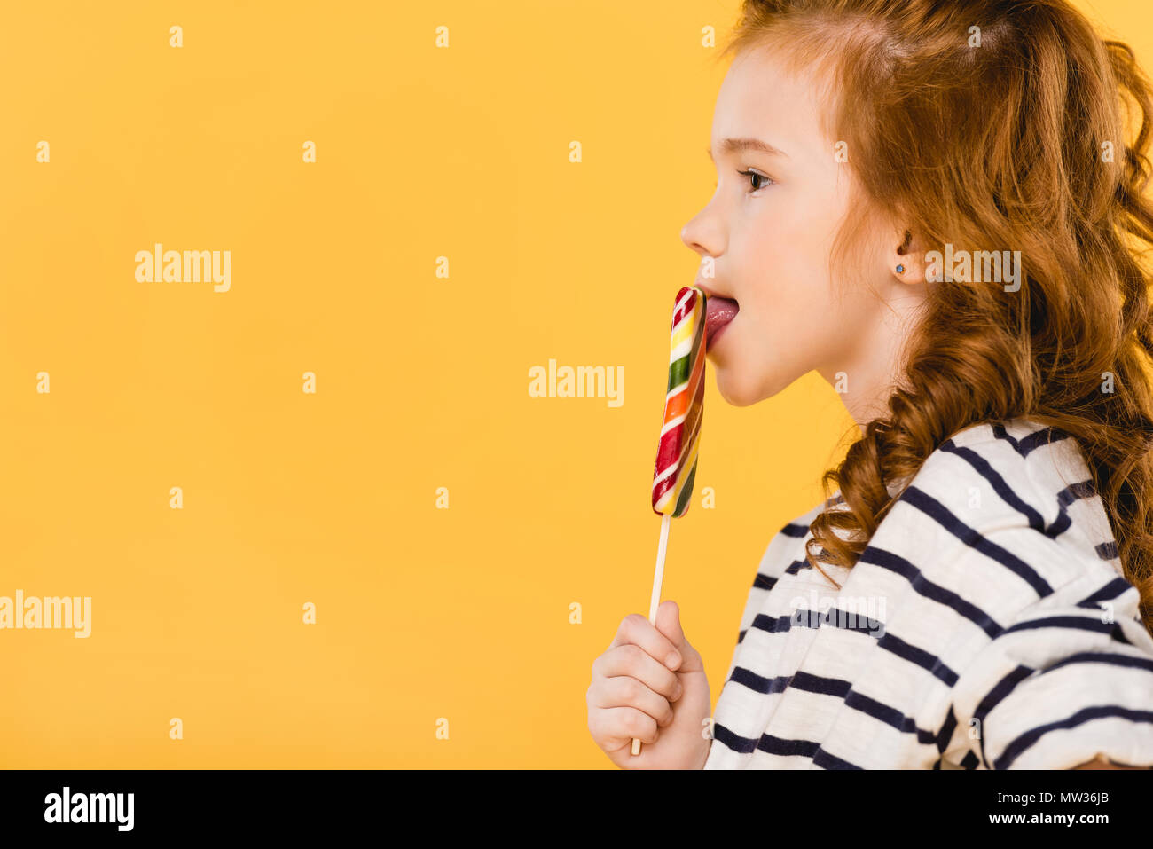 side view of preteen child eating lollipop isolated on yellow Stock Photo