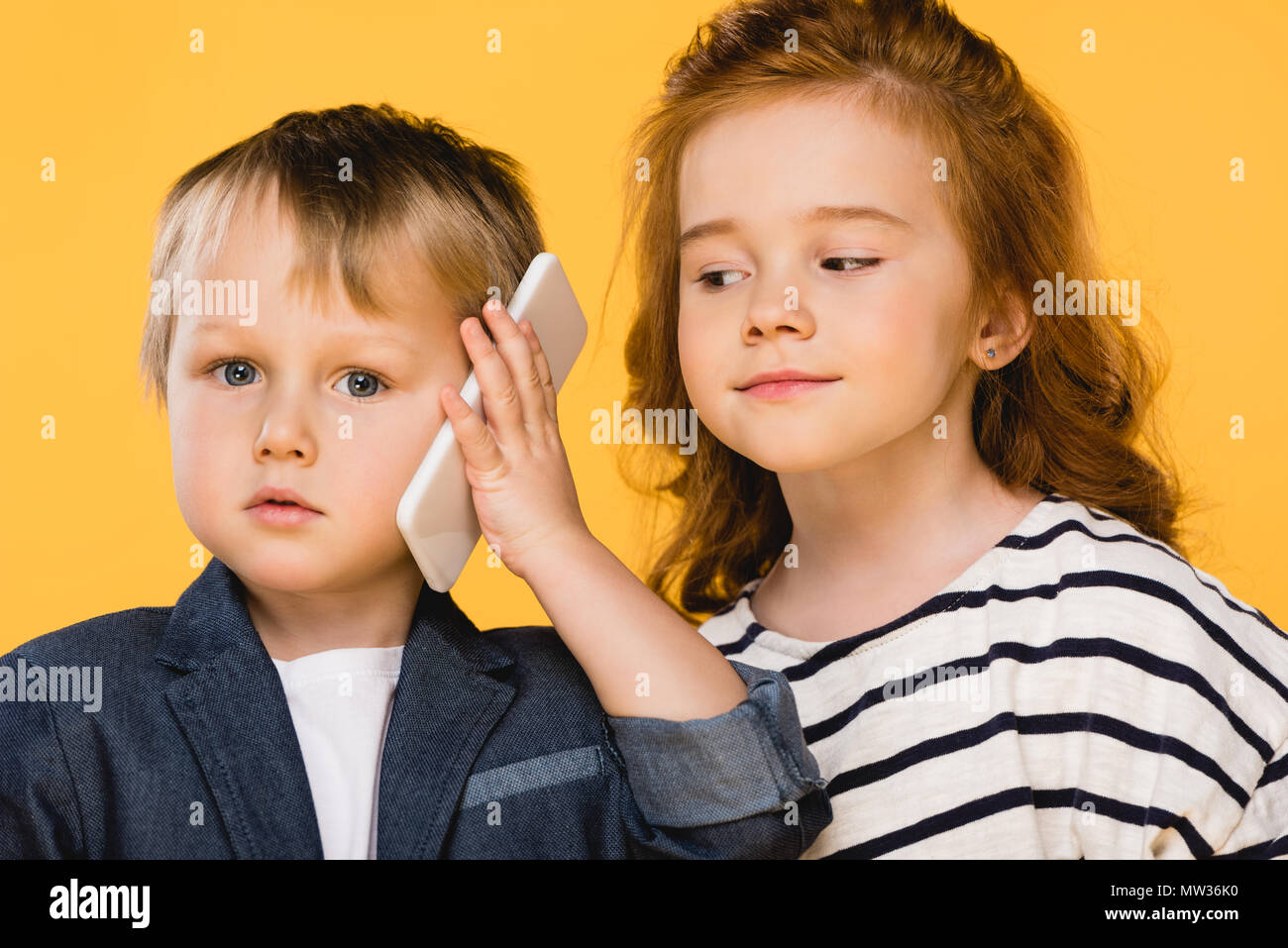 portrait of little boy talking on smartphone with friend near by isolated on yellow Stock Photo