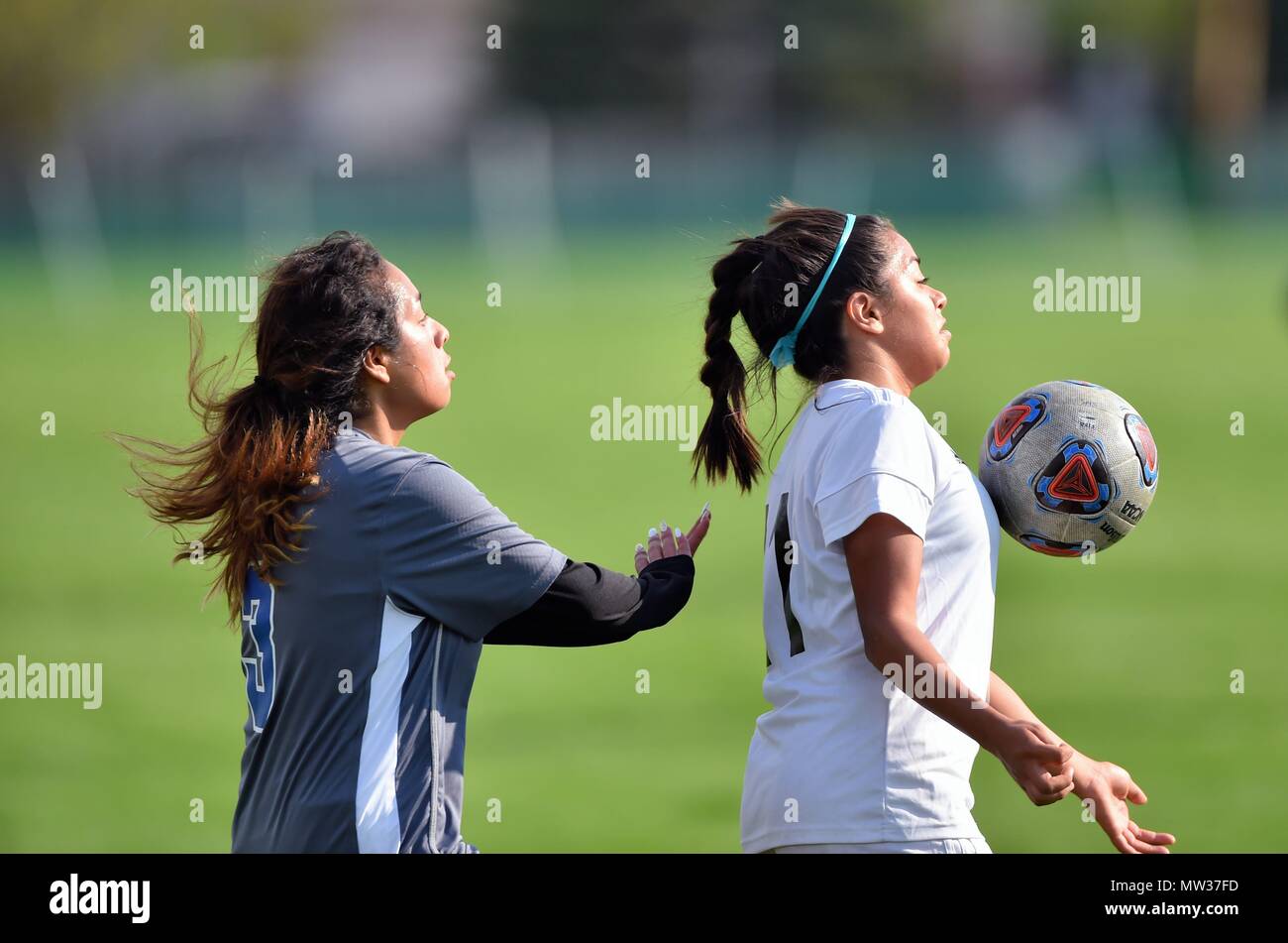 High school midfielder playing a ball off her body in front of an opponent during a conference match. USA. Stock Photo