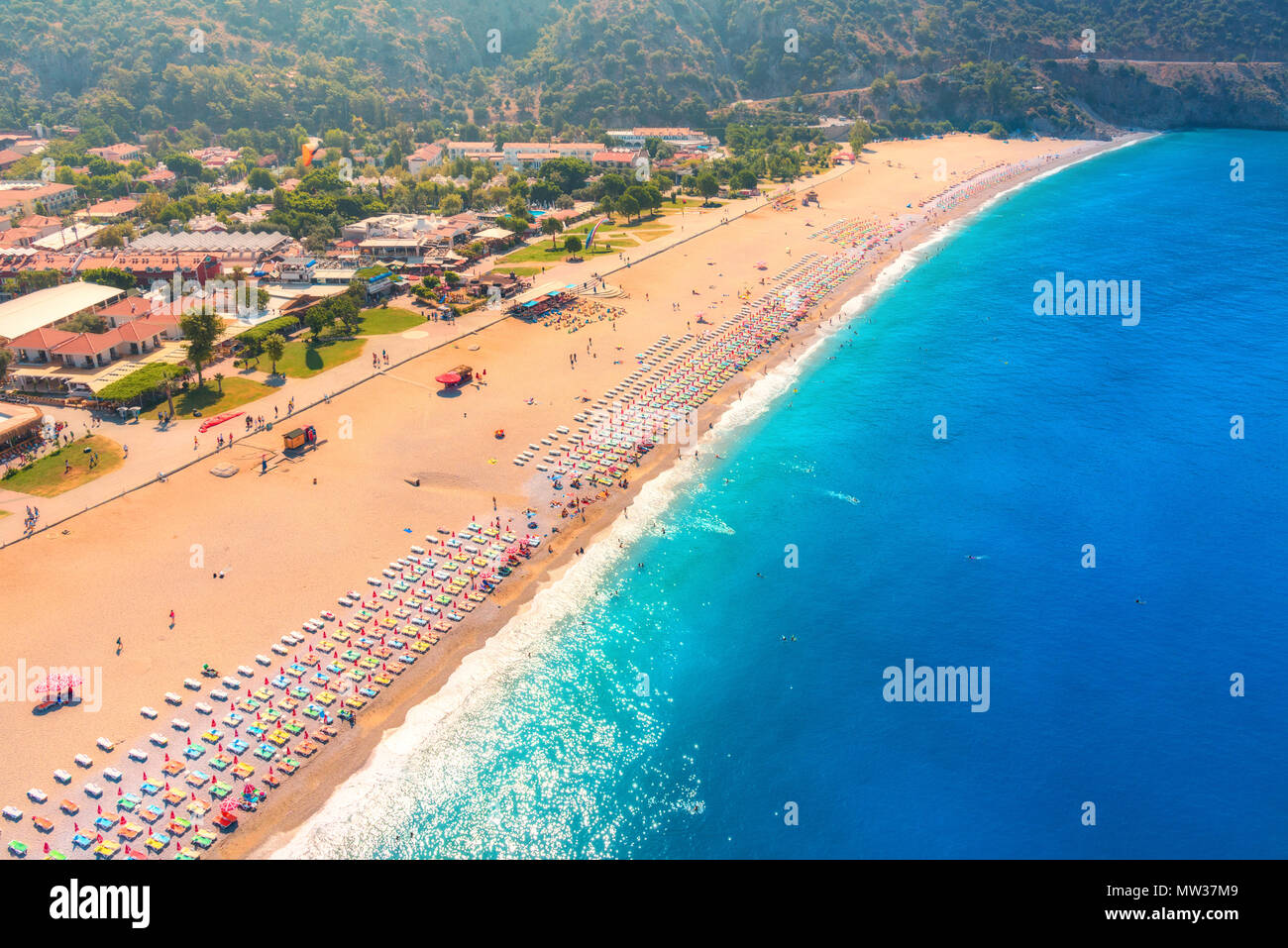 Aerial view of sandy beach with colorful chaise-lounges and blue sea in sunny bright day in Oludeniz, Turkey. Top view. Seascape with seashore, azure  Stock Photo