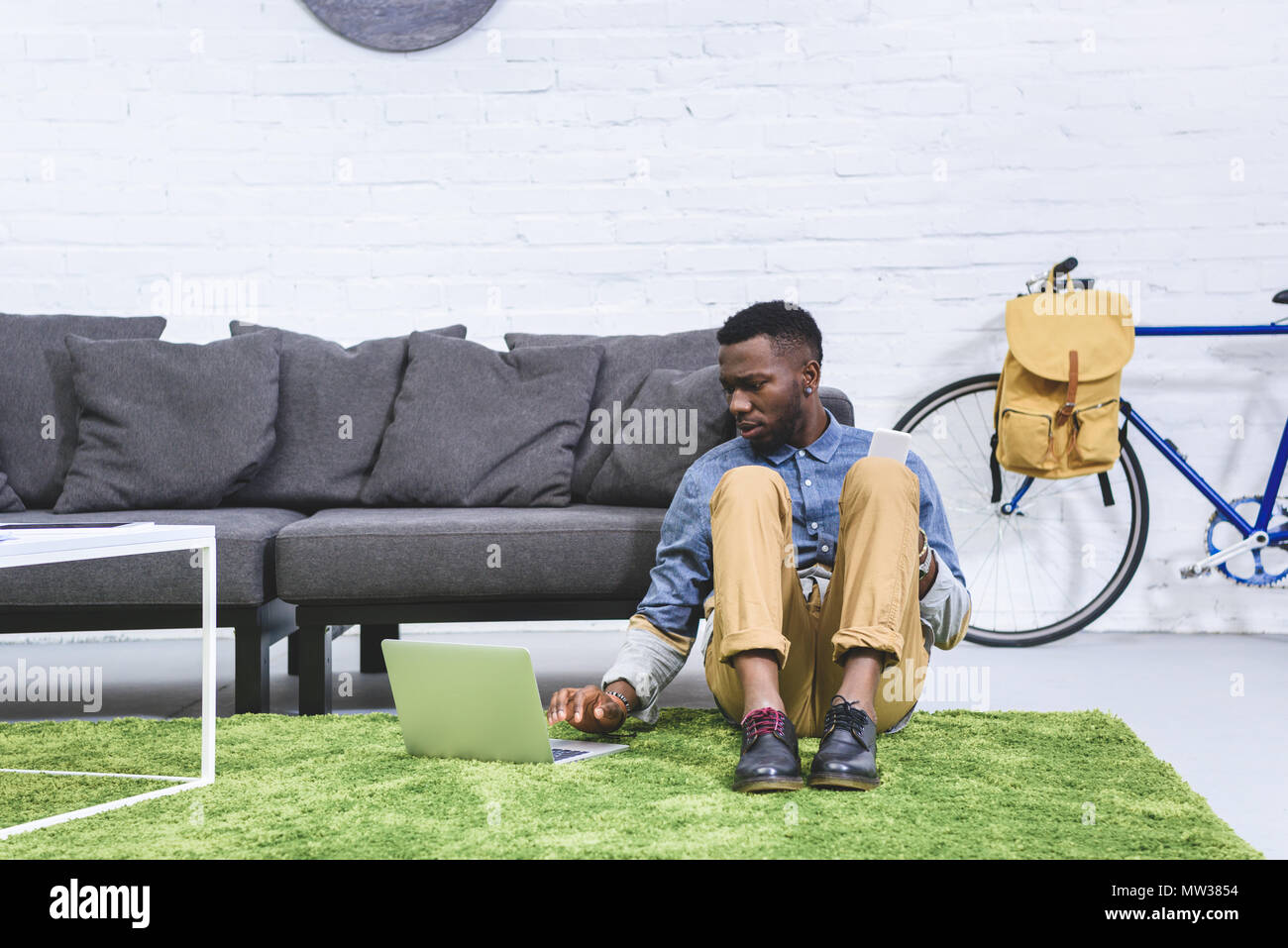 African american man working on laptop while sitting on floor by sofa ...