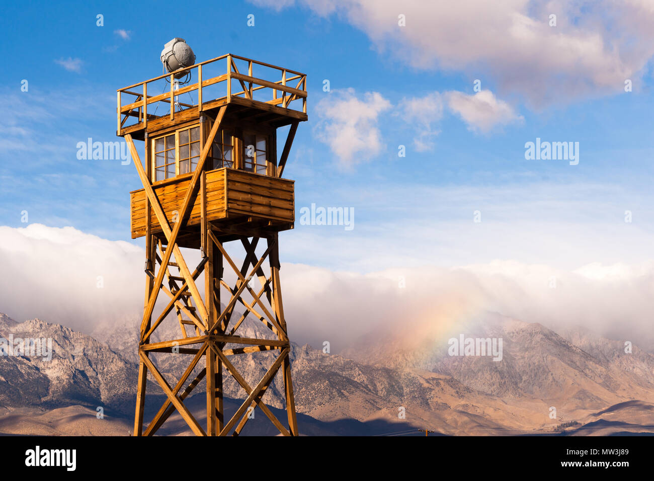 A rainbow is forming in the Sierra Nevada Mountains behind a guard tower at Manzanar Stock Photo
