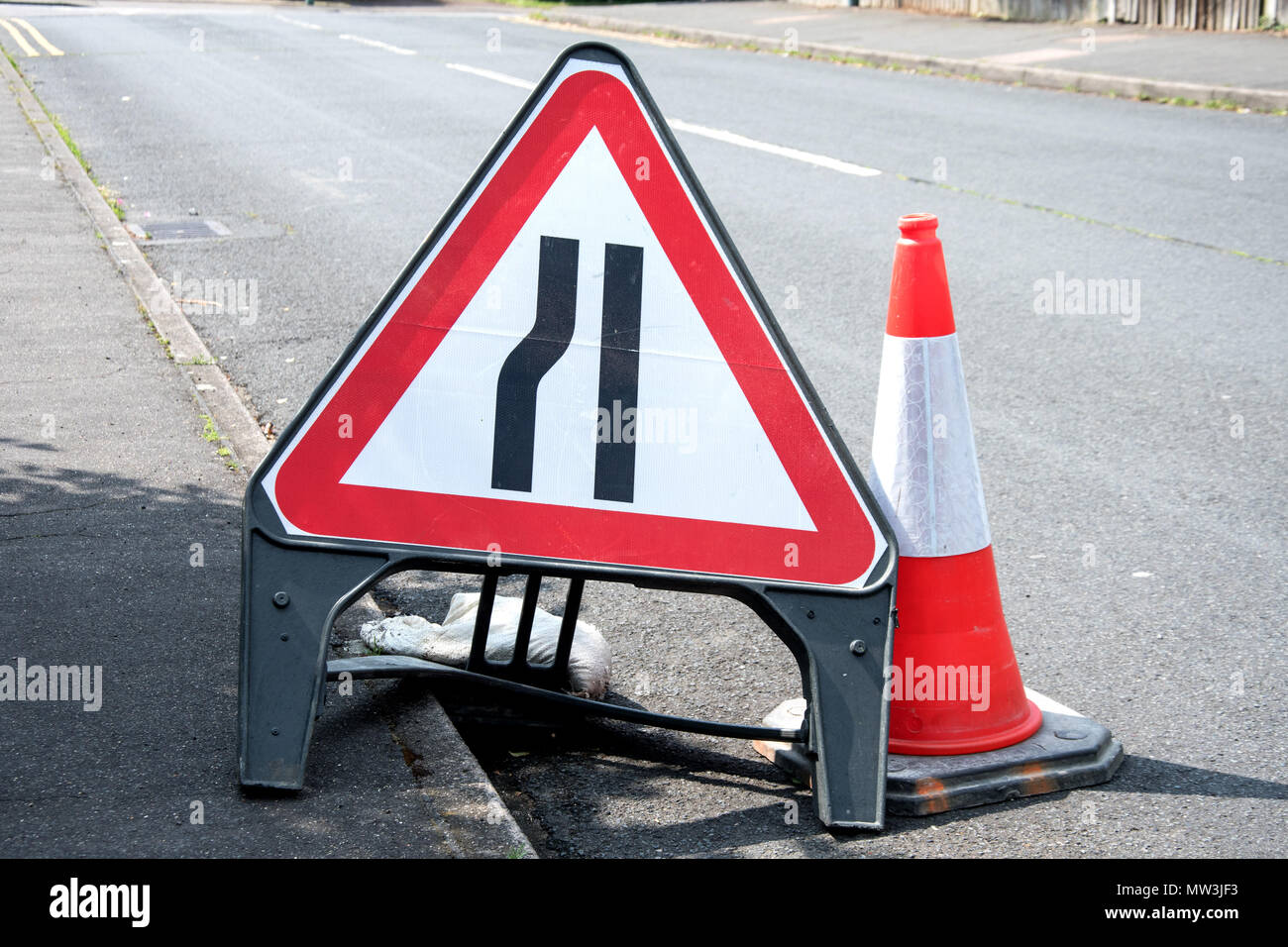 Road sign in UK. Road narrows from left, and a road cone Stock Photo