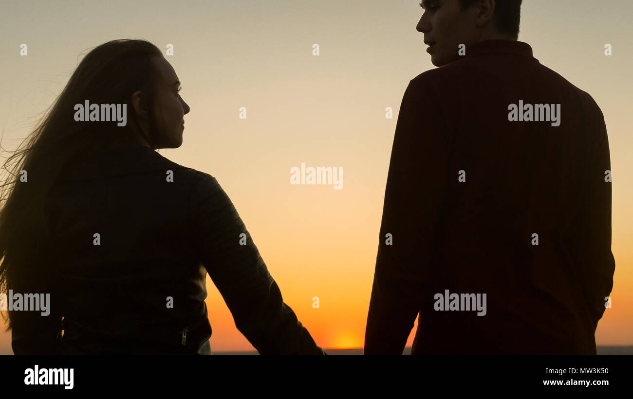 Loving young couple holding hands looking each other at amazing sunset ...