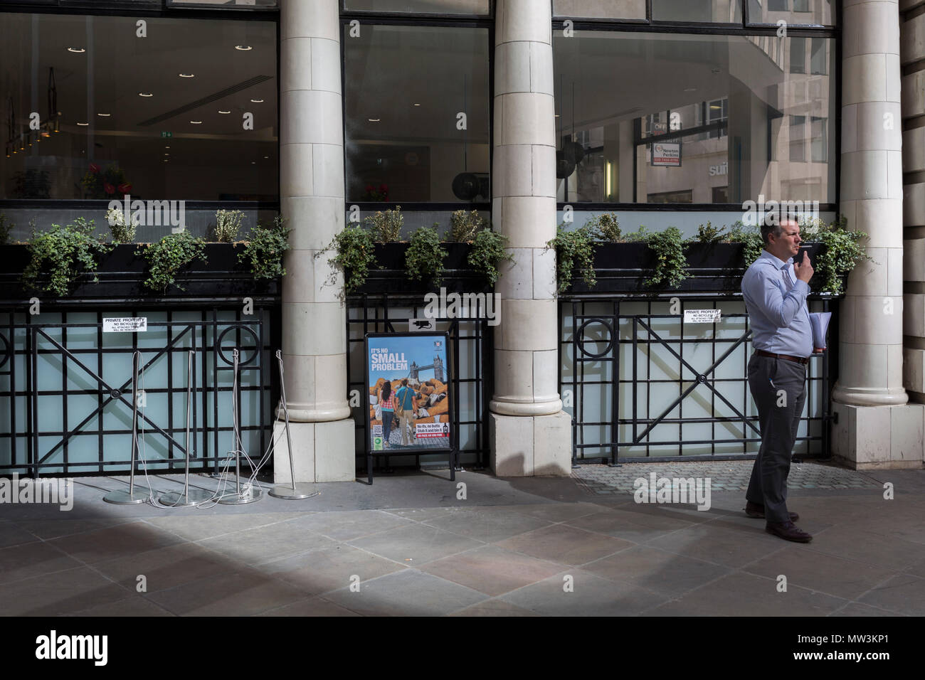 A businessman takes a cigarette break next to a sign explaining the problem of dropped cigarette butts in the City of London, the capital's financial district aka the Square Mile, on 17th May 2018, in London, UK. Stock Photo