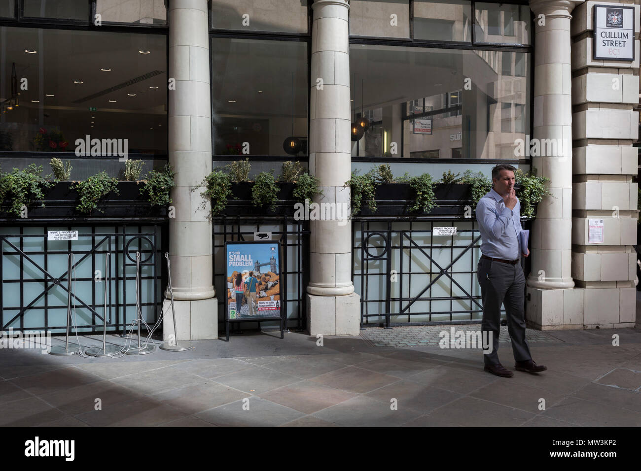 A businessman takes a cigarette break next to a sign explaining the problem of dropped cigarette butts in the City of London, the capital's financial district aka the Square Mile, on 17th May 2018, in London, UK. Stock Photo