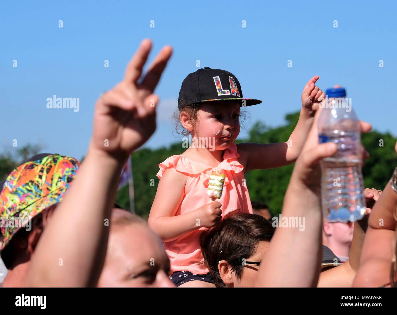 Young child wearing baseball cap on her father's shoulders in a crowd enjoying Common People Music festival May 27 2018 Stock Photo