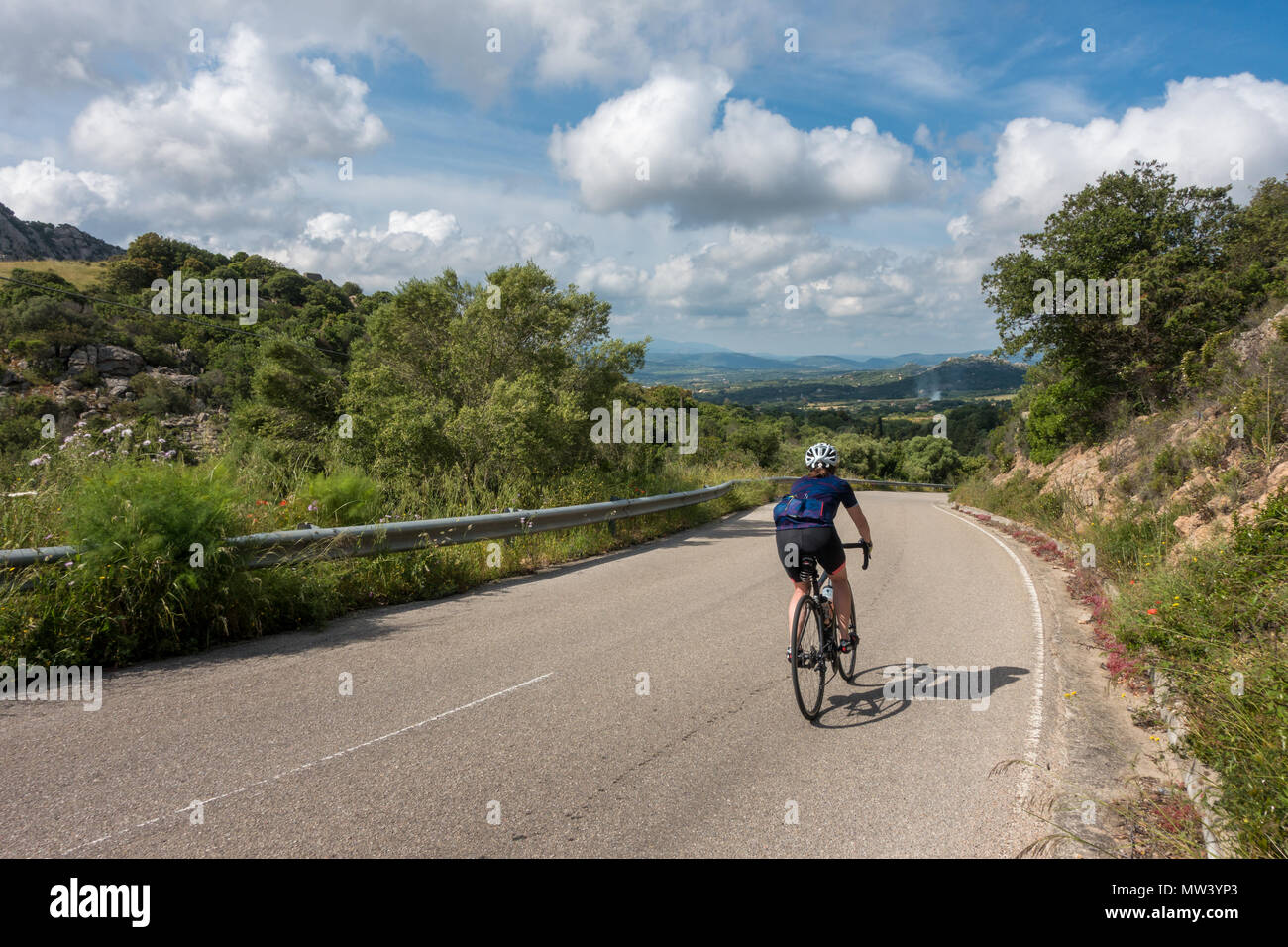 Female cyclist riding a bike downhill through the beautiful countryside of Sardinia. Stock Photo