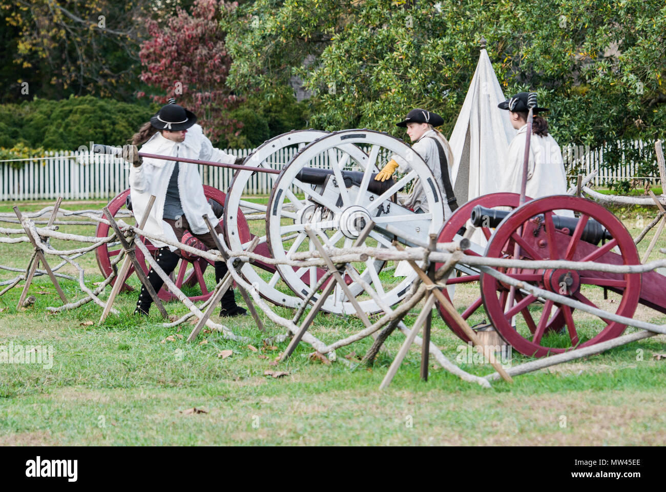 Three colonials preparing cannons to fire at close of tourist day in Colonial Williamsburg, Virginia. Men are wearing white coats & black tricorn hats Stock Photo