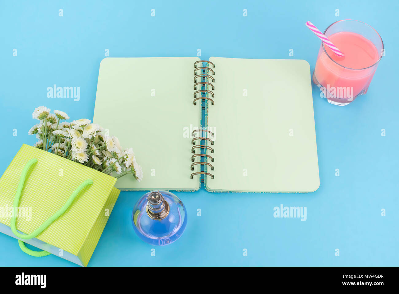 Open notebook for records lies on the surface of the cocktail pink glass tube bouquet of chrysanthemums perfume. The pastel blue background copy space Stock Photo