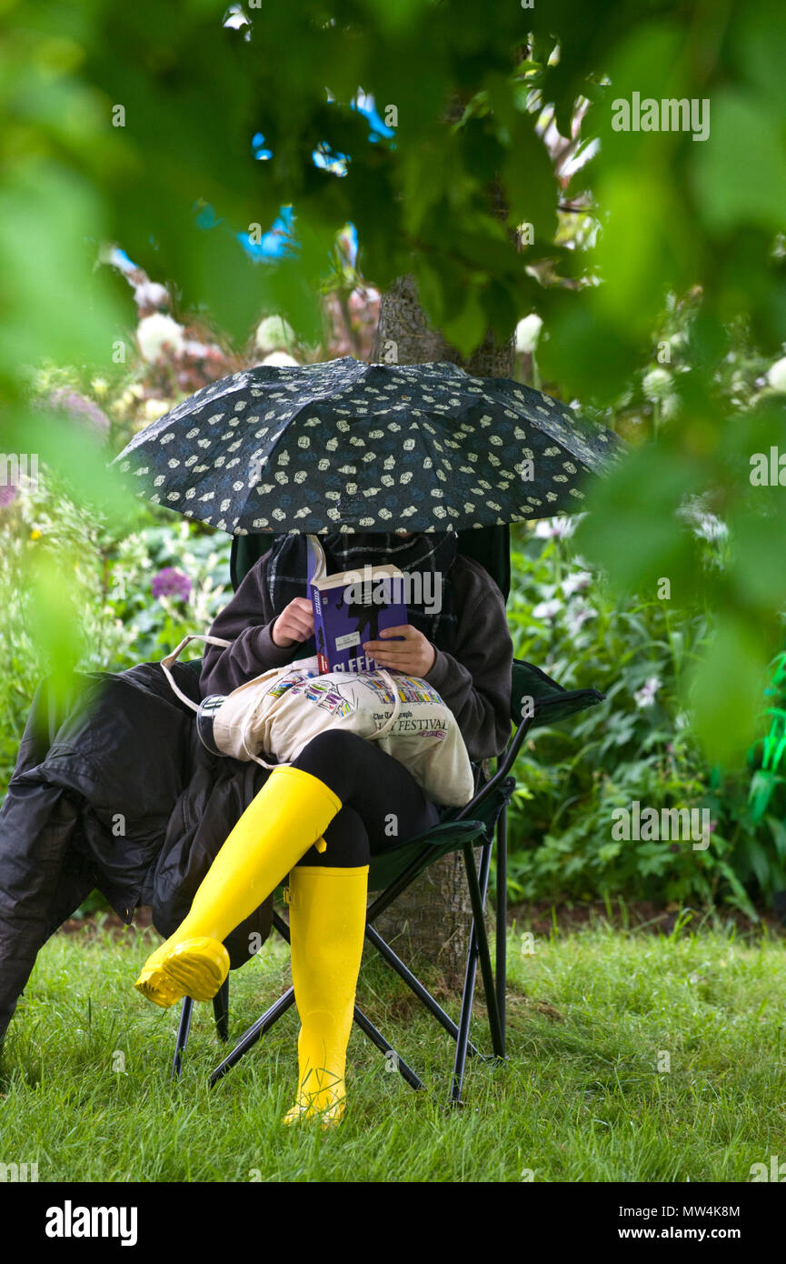 Woman reading a book with umbrella & wearing yellow wellies sat under a tree in the garden area at Hay Festival 2018 Hay-on-Wye Powys Wales UK Stock Photo