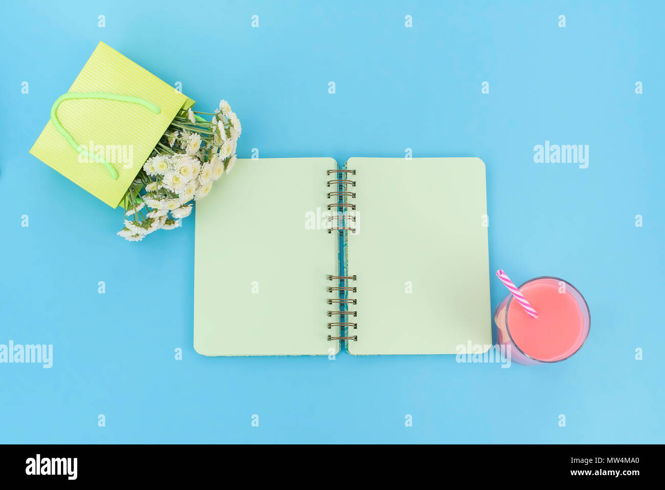 Open notebook for records lies on the surface of the cocktail pink glass tube bouquet of chrysanthemums. The pastel blue background copy space Stock Photo