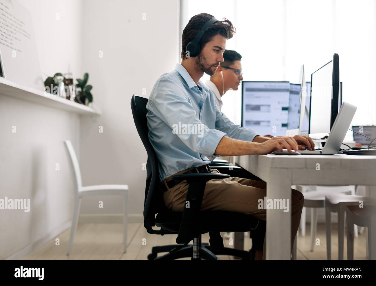 Software developers sitting at office working on computers wearing headphones. Application developer working on a laptop in office. Stock Photo