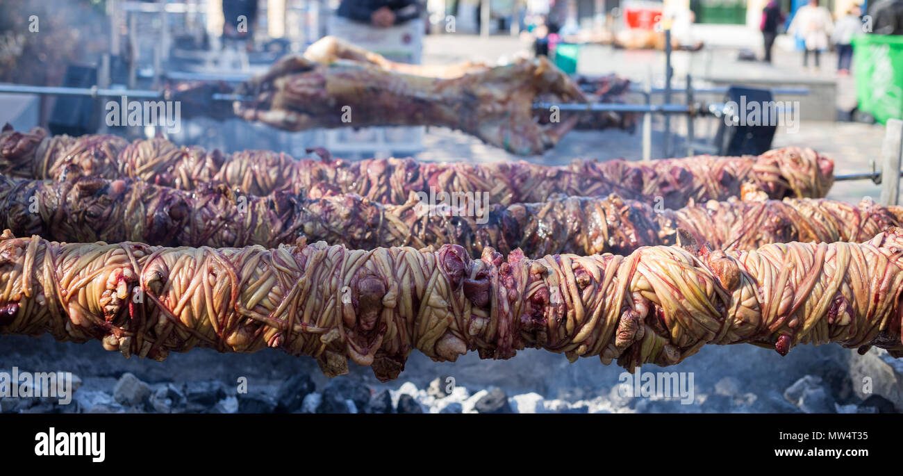 Kokoretsi, kokorech, kokorec and lamb, sheep grilling on skewers outdoor over charcoals fire. Close up view, blurred people and street background, ban Stock Photo