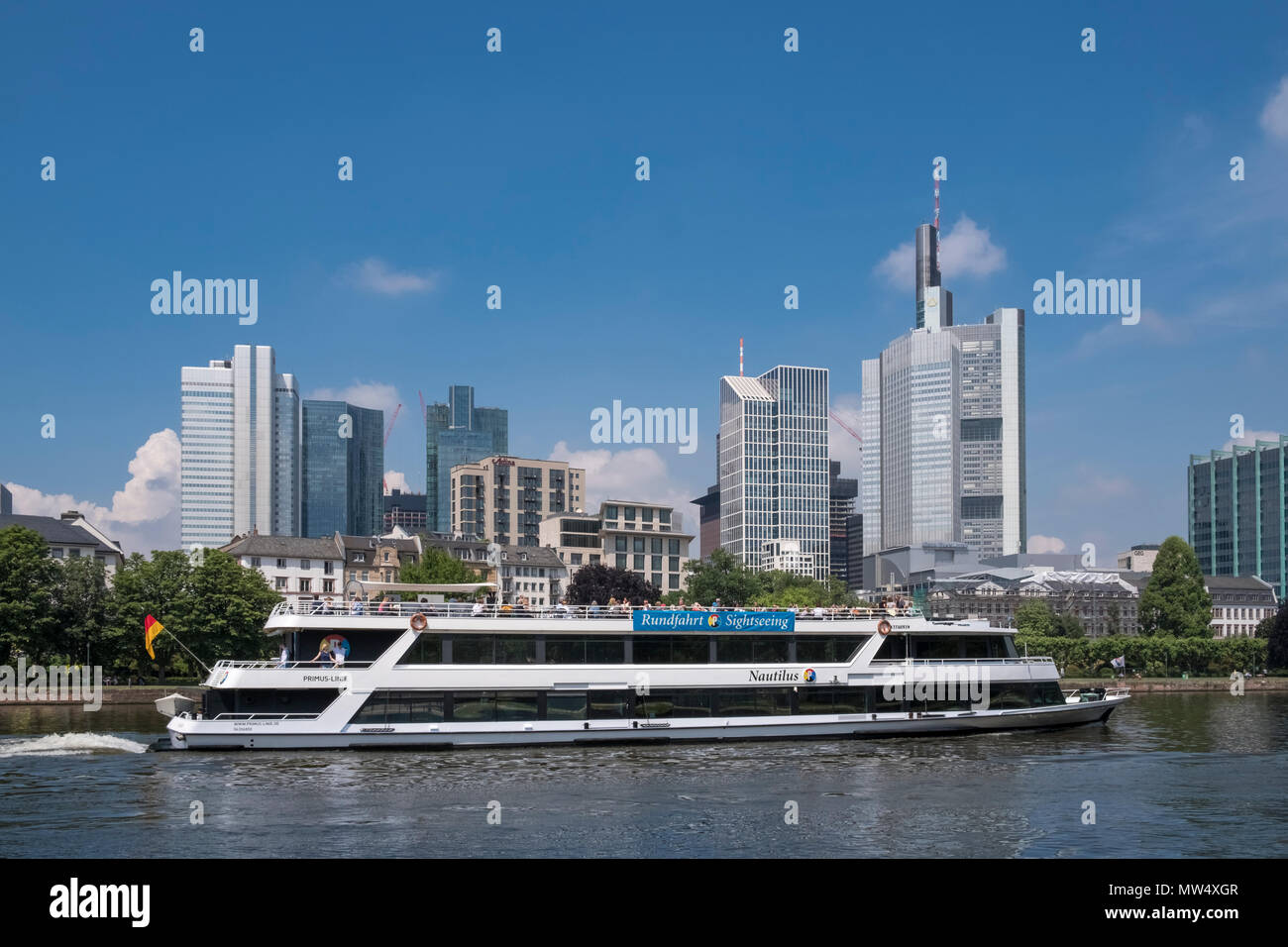An opentop rivercruise boat takes tourists along the river Main to enjoy the City of Frankfurt am Main modern architecture skyline, Germany. Stock Photo