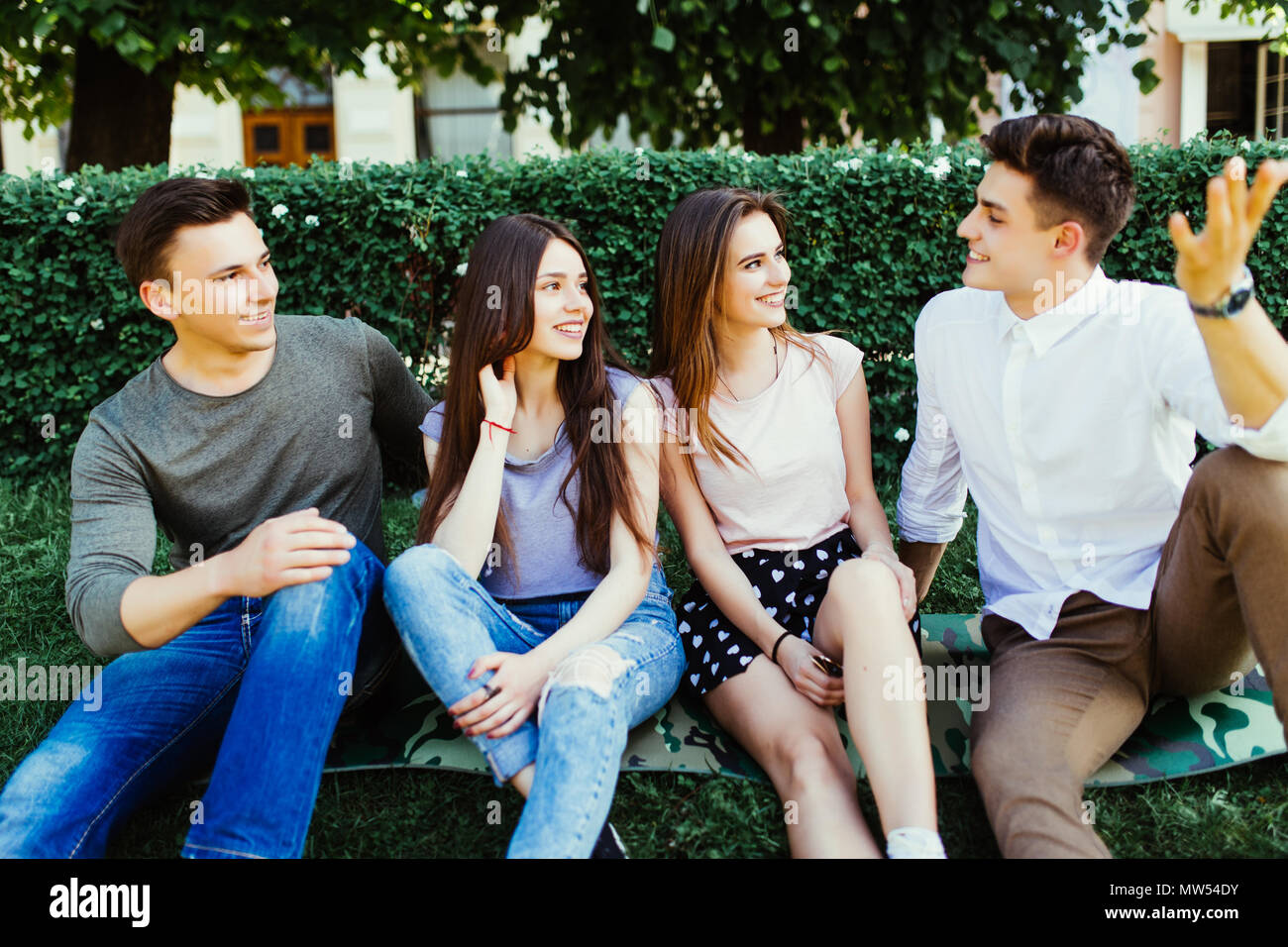 Group of four young friends in an urban park sitting on the grass in the  summer sunshine laughing and joking Stock Photo - Alamy