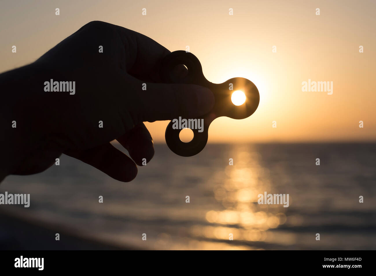Siluete of hand with fidget spinner at sunset on the sea, stress relieving toy. Stock Photo