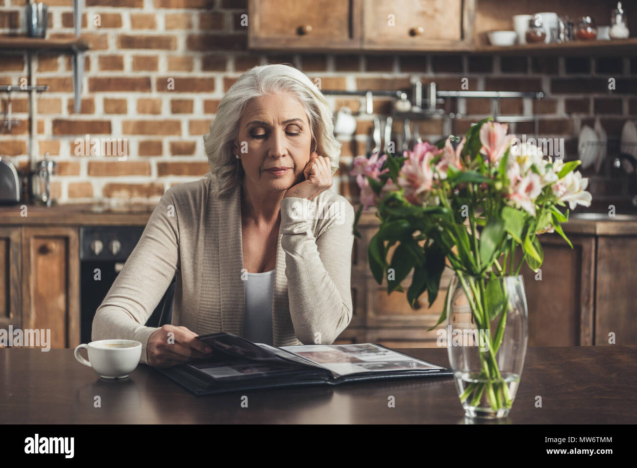 Portrait of senior woman sitting at kitchen table and looking at photo ...