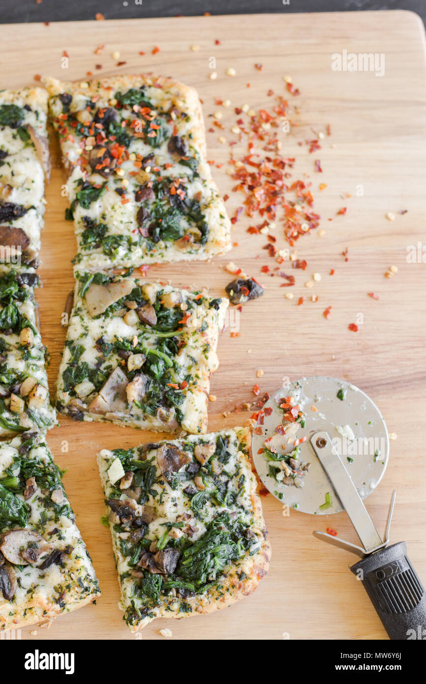 Steaming hot Detroit style pizza with cheese, spinach and mushroom toppings, season with red pepper flakes and cut to squares. Stock Photo