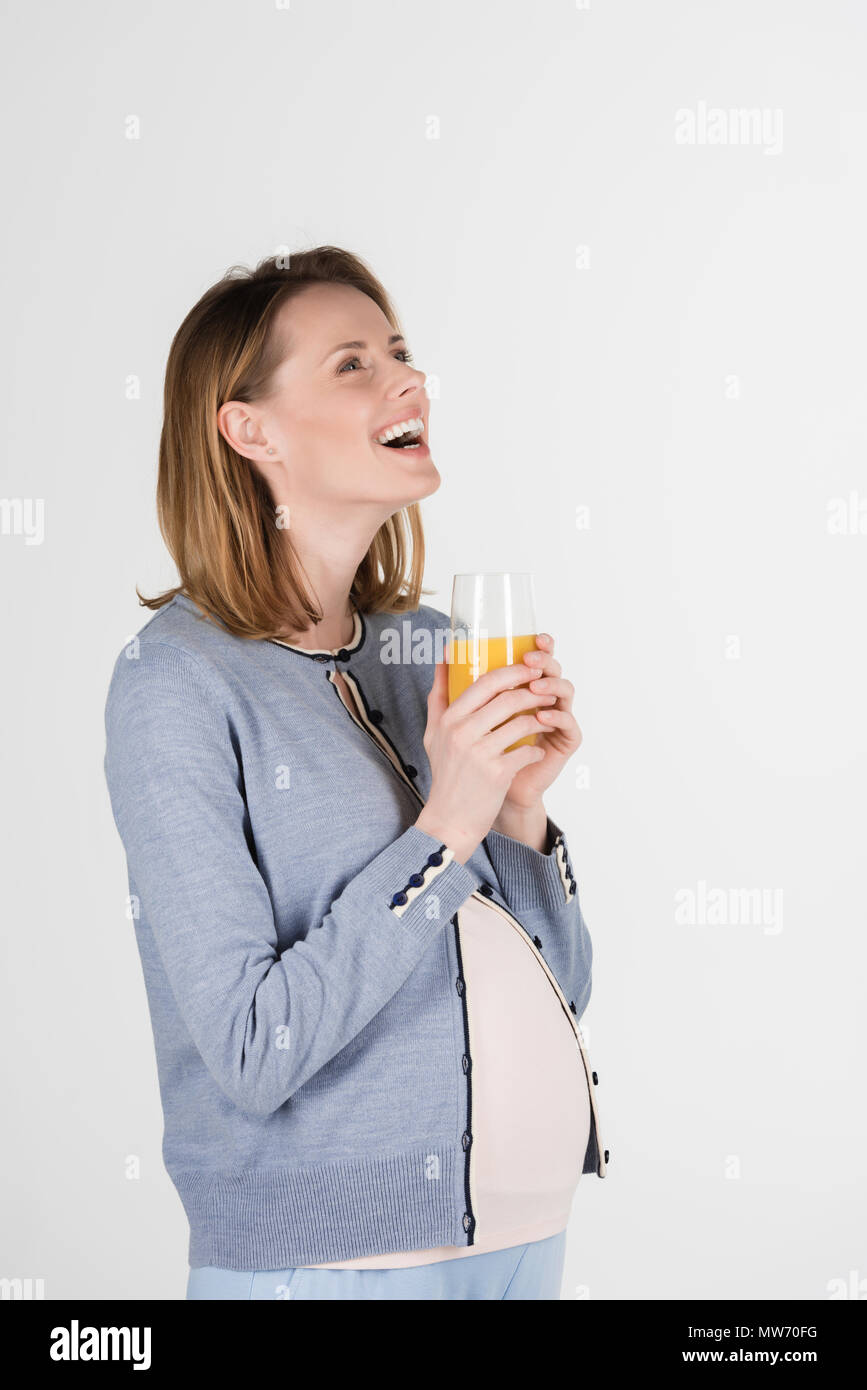 portrait of young pregnant woman posing with glass of juice in studio ...