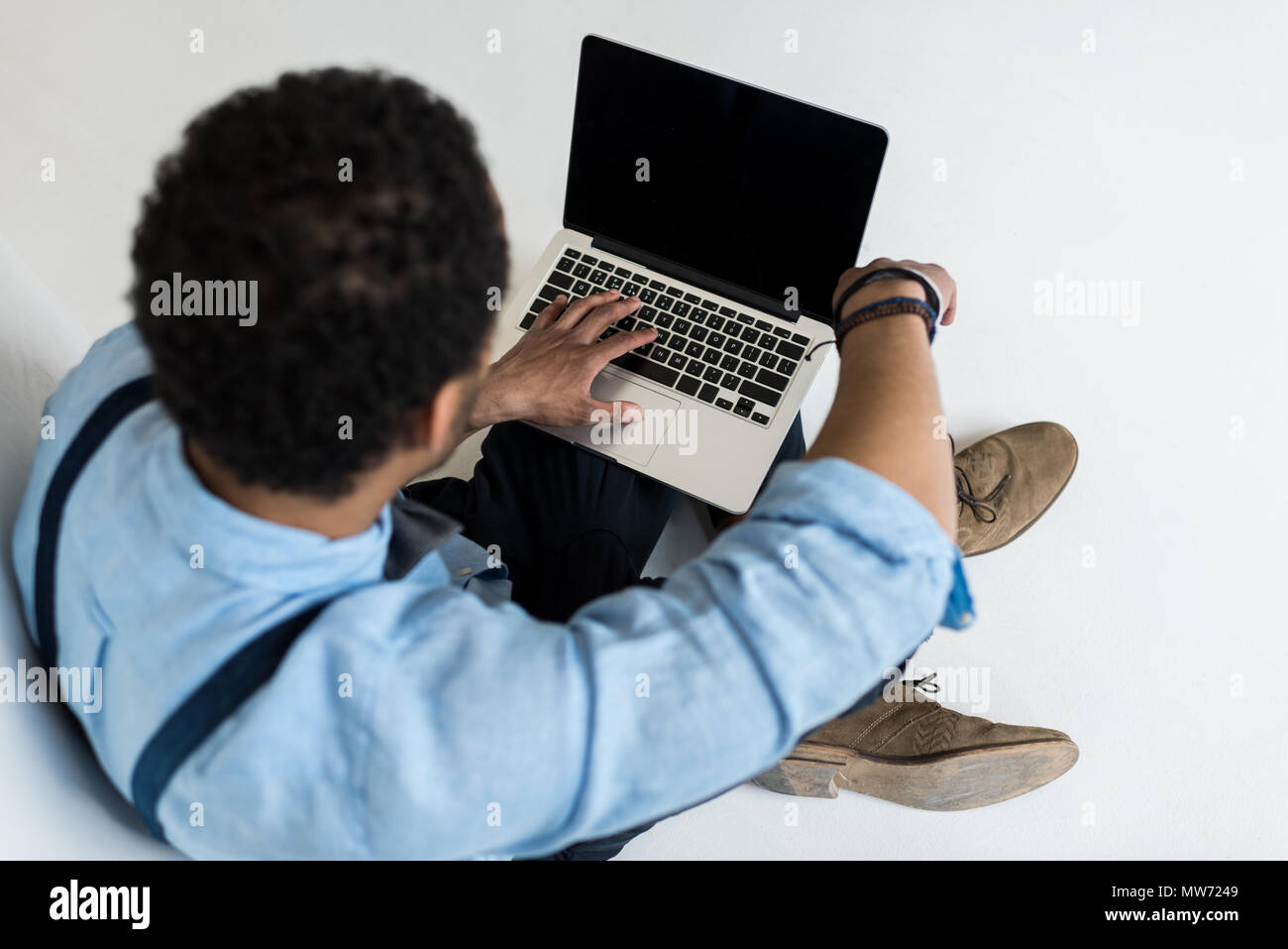 High angle view of young man sitting and using laptop with blank screen ...