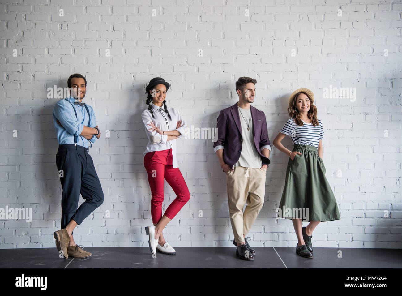 young multiethnic friends posing in stylish clothes near brick wall Stock Photo