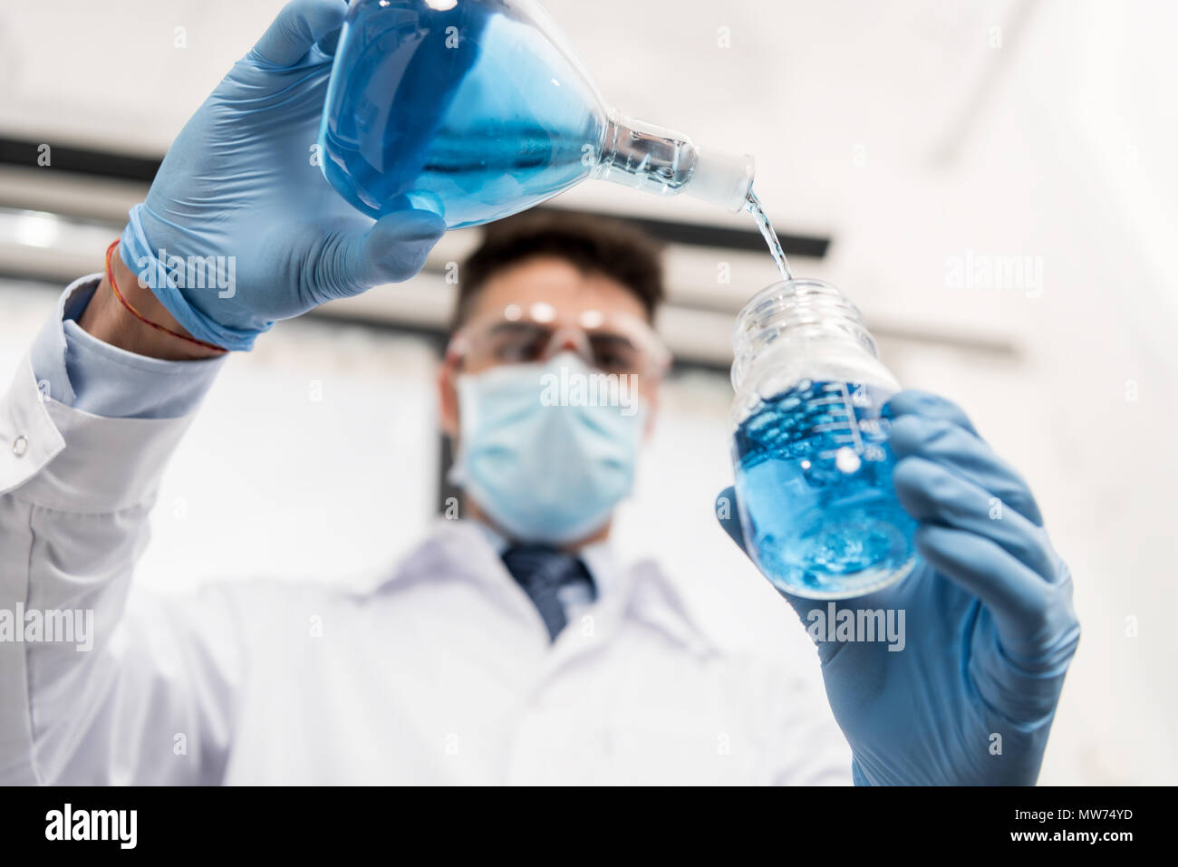 young professional scientist in sterile mask, pouring reagent into jar in laboratory Stock Photo