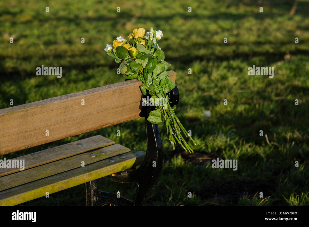 A bunch of flowers have been tied to a wooden bench in memory of a loved one. Stock Photo
