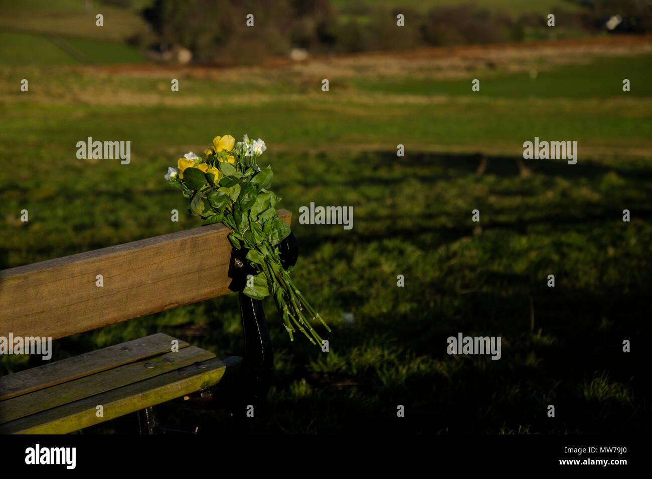 A bunch of flowers have been tied to a wooden bench in memory of a loved one. Stock Photo