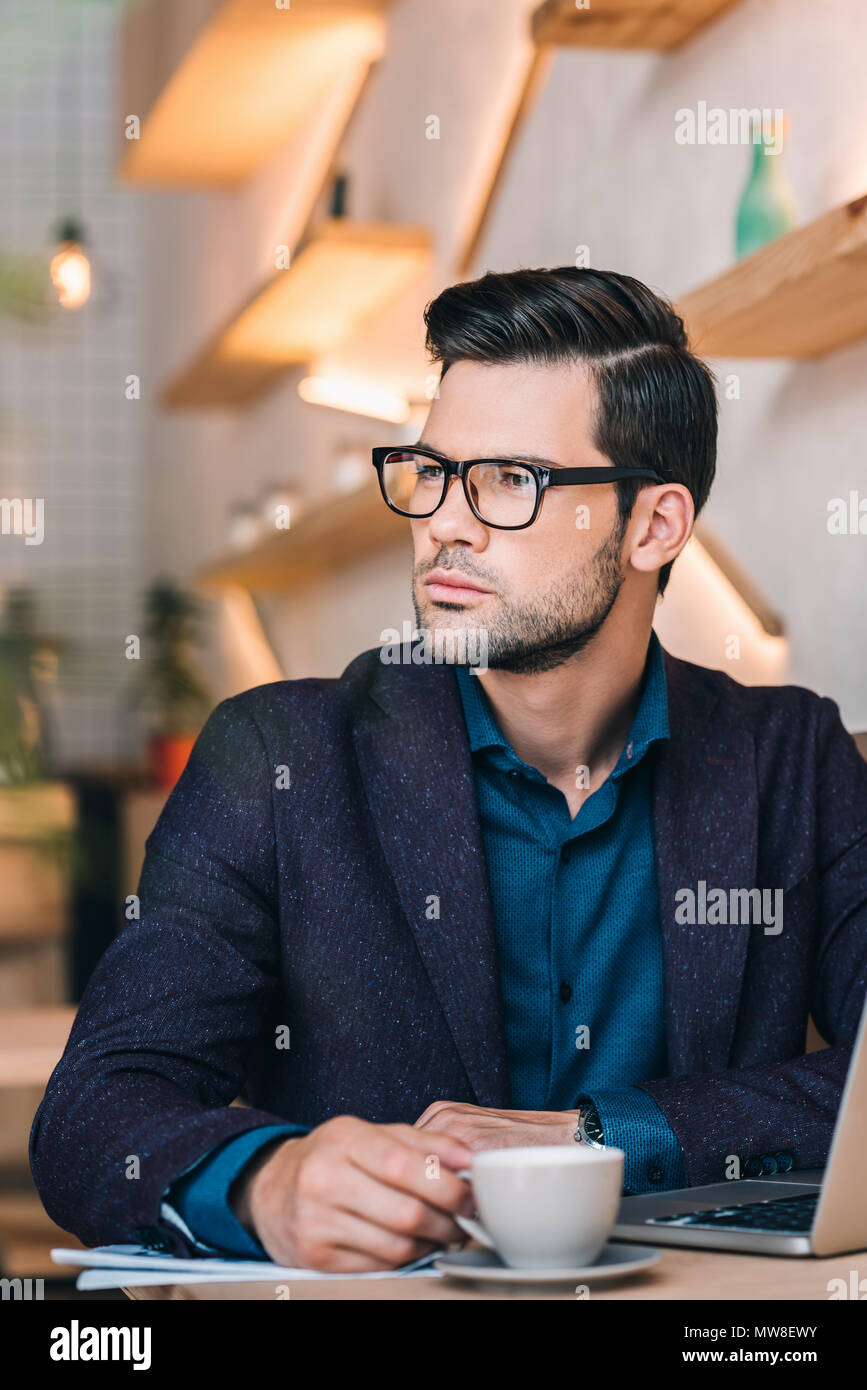 portrait of pensive businessman looking away while sitting at table with laptop in cafe Stock Photo